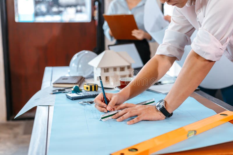 Engineers holding a pen pointing to a building and  drawing outlay construction plan as guide for builders with details. Engineer