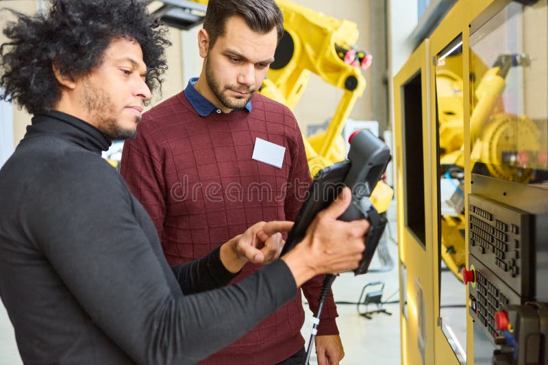 Engineers programming industrial robot with control panel for precision automation in manufacturing plant stock photography