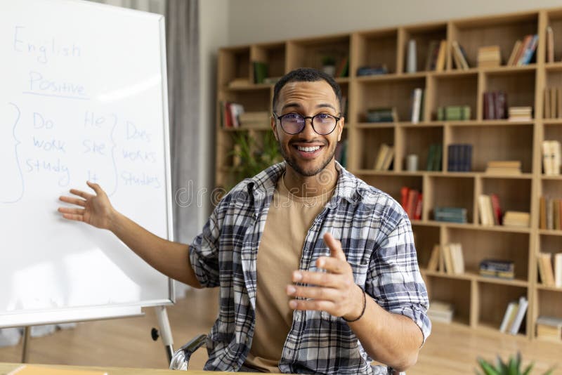 English course. Arab male teacher having foreign language class sitting near whiteboard, talking and smiling to camera royalty free stock photos