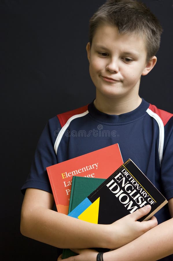 Portrait of a young teenage boy holding his school English language books, making funny face. Black background. Boring kid white stock images, royalty-free photos and pictures