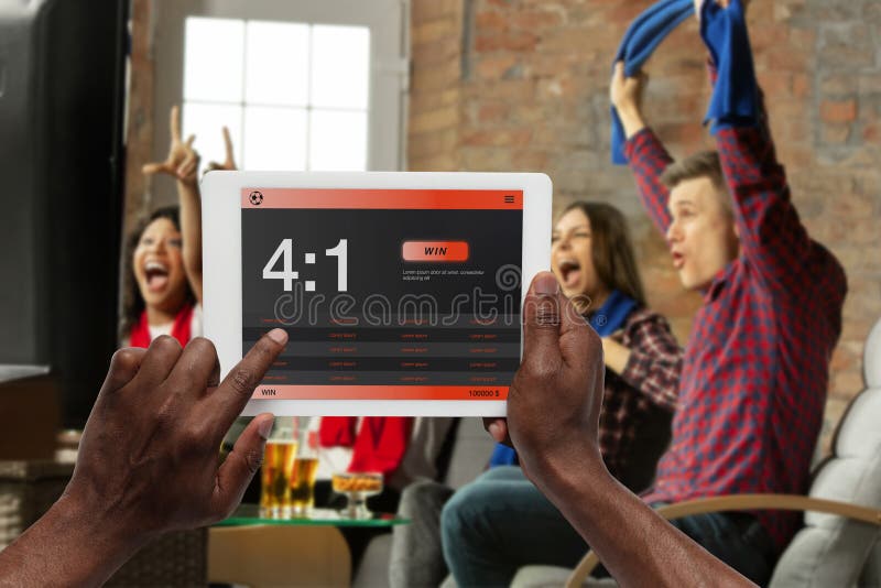 Device screen with mobile app for betting and score. Device with match results on screen, excited fans on background during match. Gambling, betting, sport, finance, modern technologies concept. Device screen with mobile app for betting and score. Device with match results on screen, excited fans on background during match. Gambling, betting, sport, finance, modern technologies concept.