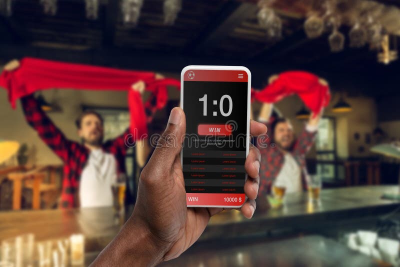 Device screen with mobile app for betting and score. Device with match results on screen, excited fans on background during match. Gambling, betting, sport, finance, modern technologies concept. Device screen with mobile app for betting and score. Device with match results on screen, excited fans on background during match. Gambling, betting, sport, finance, modern technologies concept.