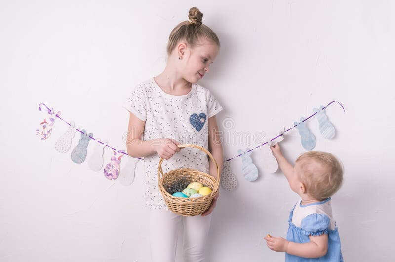 Enhorabuena en Pascua feliz: la muchacha está sosteniendo una cesta con los huevos pintados al lado de la pared blanca imagenes de archivo Enhorabuena en Pascua feliz: la muchacha está sosteniendo una cesta con los huevos pintados al lado de la pared blanca imagenes de archivo