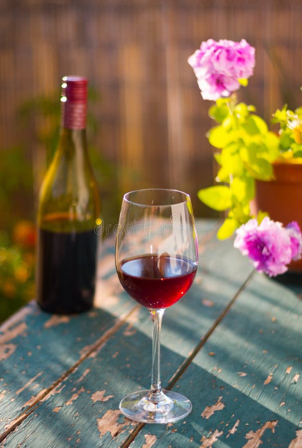 Enjoying a glass of red wine in the own garden. Rustic, old table and evening sun, summertime