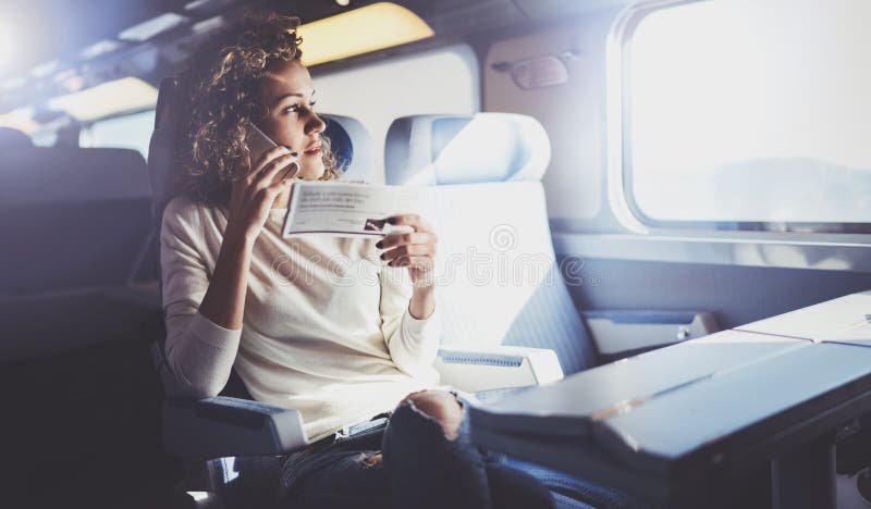 Enjoying travel concept. Young pretty woman tourist traveling by the train sitting near the window using smartphone.