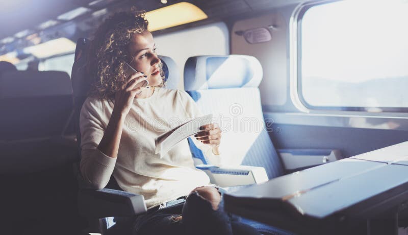 Enjoying travel concept. Young pretty woman tourist traveling by the train sitting near the window using smartphone.