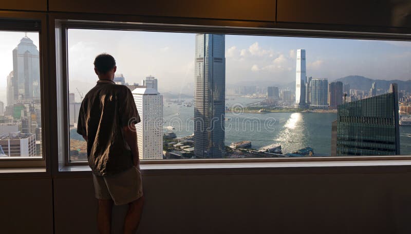 Un uomo che sta in alto, sopra le trafficate strade di Hong Kong, e gode l'ampia vista della baia e della zona circostante e gli edifici moderni.