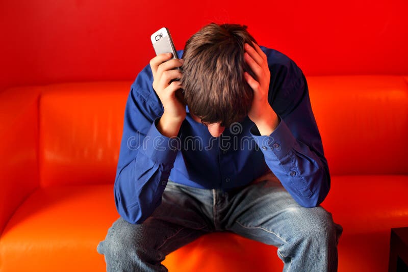 Sad teenager sitting on the sofa with the mobile phone. Sad teenager sitting on the sofa with the mobile phone