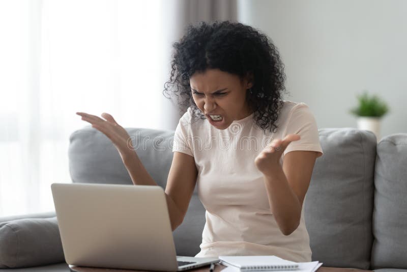 Enojado subrayó a la mujer negra joven que miraba la sensación del ordenador portátil enfadada