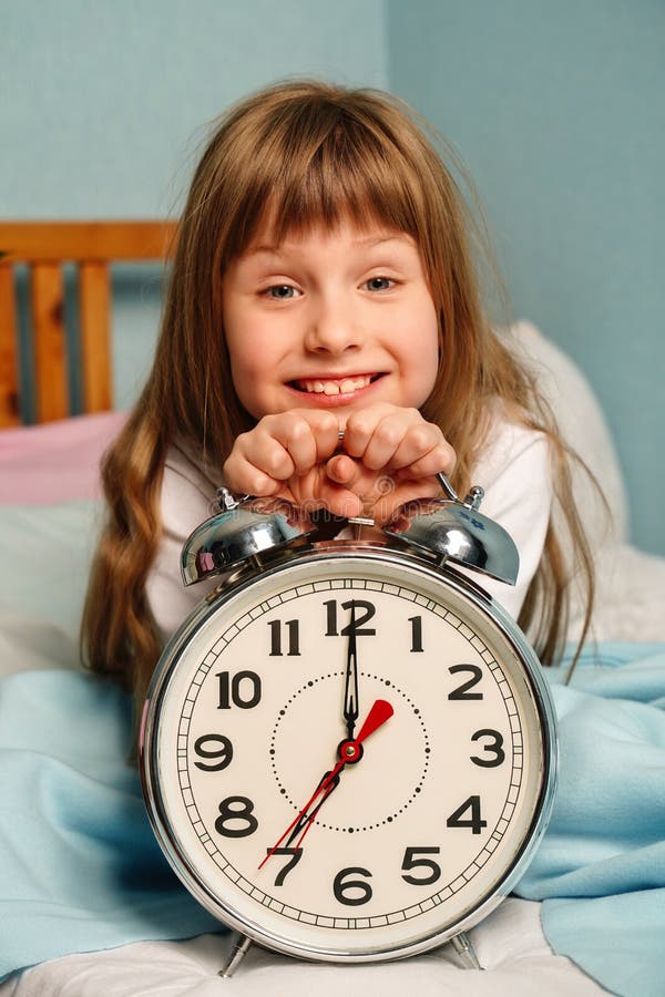Enorme sveglia nelle mani di una bambina sorridente felice nella camera da letto alle 7 del mattino. immagini stock