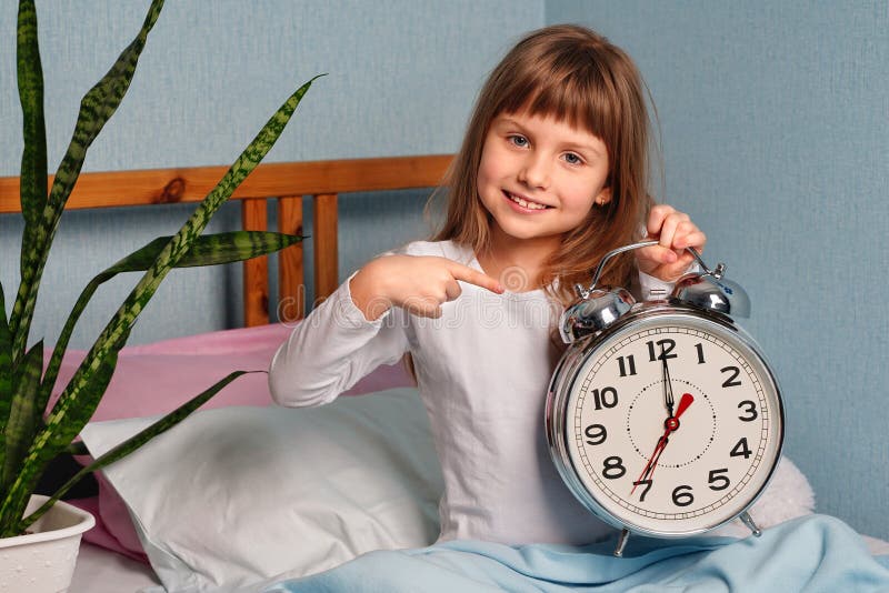 Enorme sveglia nelle mani di una bambina sorridente felice nella camera da letto alle 7 del mattino. immagini stock