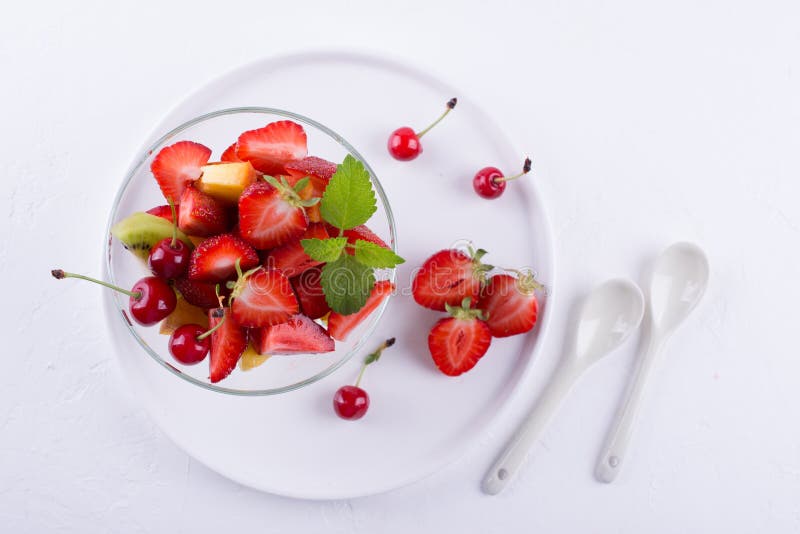 Ensalada de fruta sabrosa fresca de la mezcla en el bol de vidrio en el fondo blanco de la tabla Desayuno sano de la vitamina fotografía de archivo Ensalada de fruta sabrosa fresca de la mezcla en el bol de vidrio en el fondo blanco de la tabla Desayuno sano de la vitamina fotografía de archivo