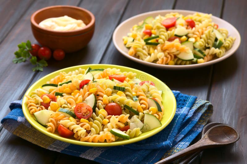 Two plates of vegetarian pasta salad made of tricolor fusilli, sweet corn, cucumber and cherry tomato with mayonnaise in the back, photographed with natural light (Selective Focus, Focus one third into the first salad). Two plates of vegetarian pasta salad made of tricolor fusilli, sweet corn, cucumber and cherry tomato with mayonnaise in the back, photographed with natural light (Selective Focus, Focus one third into the first salad)