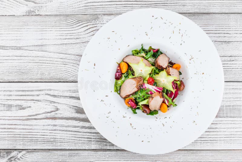 Ensalada fresca con la pechuga de pollo, el arugula, la lechuga, la coliflor, el physalis y el carambola en la placa en cierre de fotografía de archivo Ensalada fresca con la pechuga de pollo, el arugula, la lechuga, la coliflor, el physalis y el carambola en la placa en cierre de fotografía de archivo