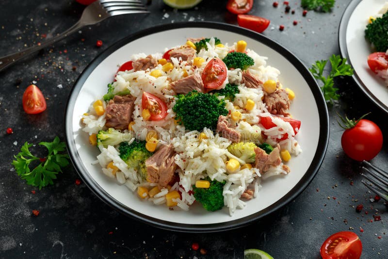Ensalada fresca del arroz del atún con maíz dulce, los tomates de cereza, el bróculi, el perejil y la cal en cuenco negro foto de archivo Ensalada fresca del arroz del atún con maíz dulce, los tomates de cereza, el bróculi, el perejil y la cal en cuenco negro foto de archivo