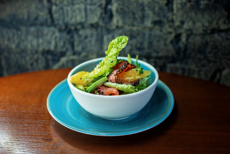 Ensalada sabrosa con el prendedero de color salmón con las verduras frescas y una rebanada de naranja en la tabla en el restauran fotos de archivo Ensalada sabrosa con el prendedero de color salmón con las verduras frescas y una rebanada de naranja en la tabla en el restauran fotos de archivo
