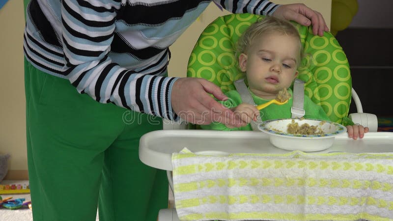 Ensam far som hjälper sin lilla barnunge att äta porridmash från skål