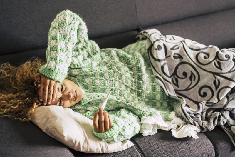 Ensam kvinna hemma som ligger på soffan och tittar på termometern med hög febertemperatur - sjuk kvinna med hårlös arkivfoto Ensam kvinna hemma som ligger på soffan och tittar på termometern med hög febertemperatur - sjuk kvinna med hårlös arkivfoto