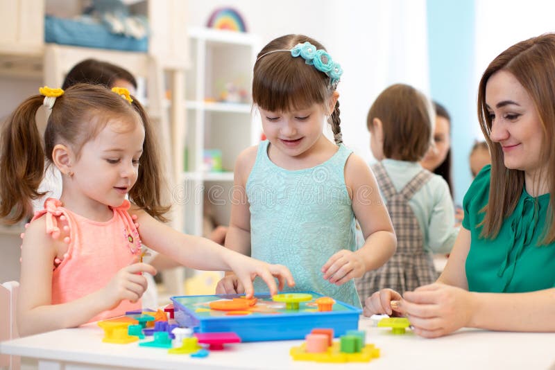 Enseignant de jardin d'enfants et enfants jouant à la trieuse de jouets dans une garderie images stock Enseignant de jardin d'enfants et enfants jouant à la trieuse de jouets dans une garderie images stock