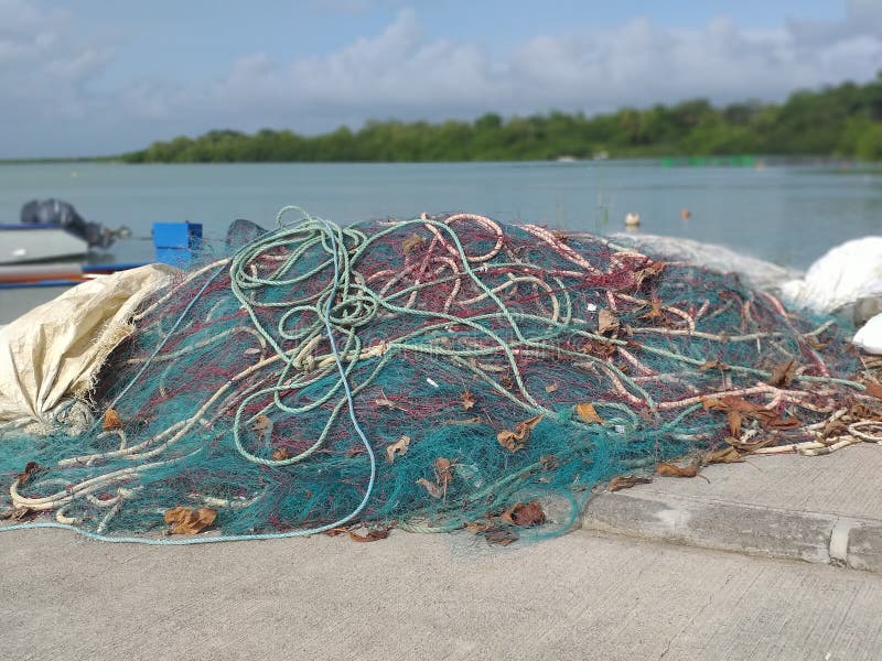 Foreground of fishing nets and ropes of different sizes and colors on a pier in the fishing port of the Caribbean town. Turquoise and calm waters. In the background vegetation. Blue sky with small white clouds. Foreground of fishing nets and ropes of different sizes and colors on a pier in the fishing port of the Caribbean town. Turquoise and calm waters. In the background vegetation. Blue sky with small white clouds.