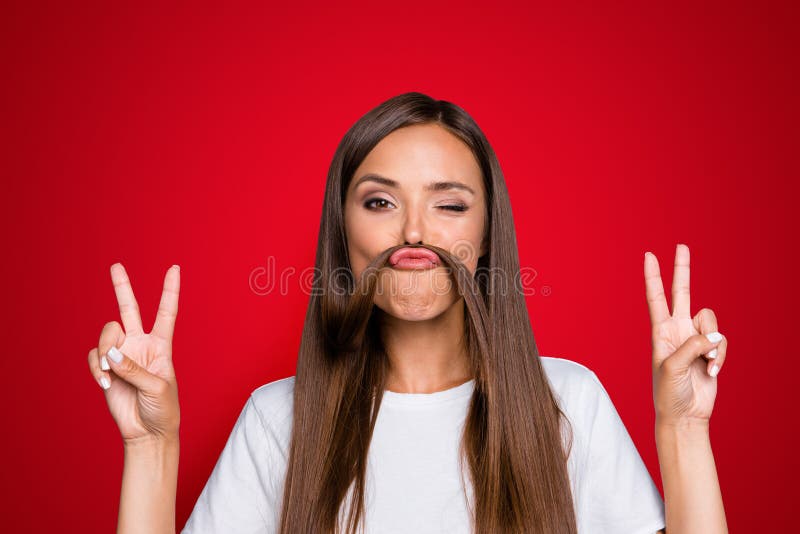 Fun prank joy entertainment concept. Close up portrait of young charming brunette shows v-sign and holds her hair over her lip like a fake mustache isolated on gray background. Fun prank joy entertainment concept. Close up portrait of young charming brunette shows v-sign and holds her hair over her lip like a fake mustache isolated on gray background.