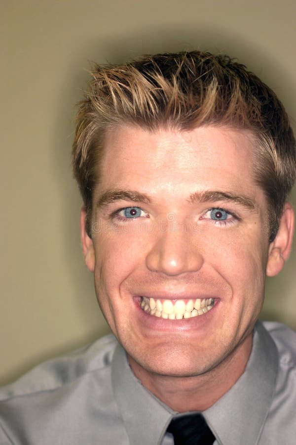 Blond hair blue eye business man with big smile wearing gray shirt and black tie against tan background. Blond hair blue eye business man with big smile wearing gray shirt and black tie against tan background