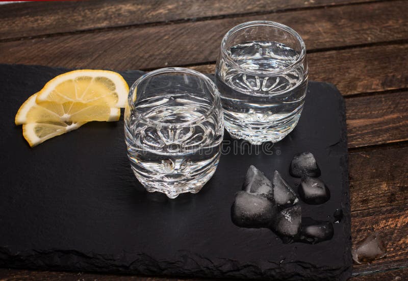Entkörnen Sie Stärkungsmittel, Wodka, oder Rum mit Eis und Zitrone auf Schieferbrett flehen an an lizenzfreie stockbilder Entkörnen Sie Stärkungsmittel, Wodka, oder Rum mit Eis und Zitrone auf Schieferbrett flehen an an lizenzfreie stockbilder
