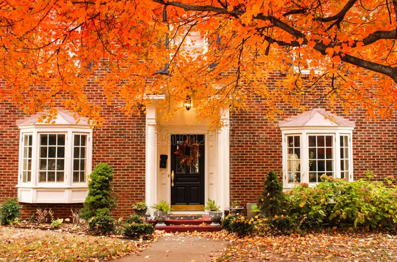 Entrada de la casa del ladrillo rojo con la guirnalda estacional en puerta y pórtico y ventanas saledizas el día del otoño con la