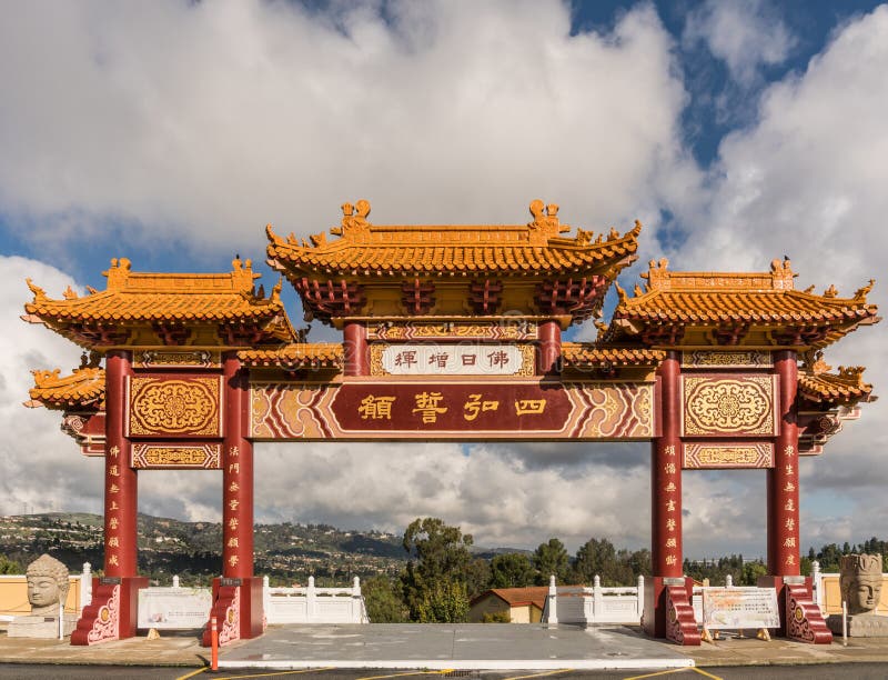 Hacienda Heights, CA, USA - March 23, 2018: Red and ochre colored Torii enrance gate to Hsi Lai Buddhist Temple under blue-white cloudscape. Mandarin characters sign. Green hills in distance. Hacienda Heights, CA, USA - March 23, 2018: Red and ochre colored Torii enrance gate to Hsi Lai Buddhist Temple under blue-white cloudscape. Mandarin characters sign. Green hills in distance.