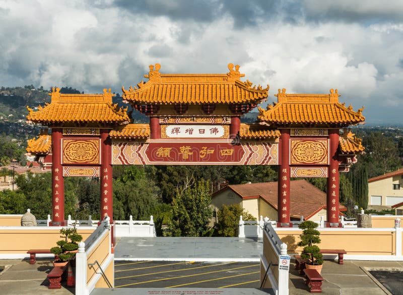 Hacienda Heights, CA, USA - March 23, 2018: Red and ochre colored Torii enrance gate to Hsi Lai Buddhist Temple under blue-white cloudscape. Mandarin characters sign. Green hills in distance. Hacienda Heights, CA, USA - March 23, 2018: Red and ochre colored Torii enrance gate to Hsi Lai Buddhist Temple under blue-white cloudscape. Mandarin characters sign. Green hills in distance.