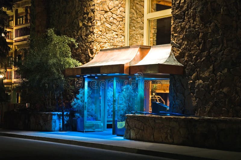 Entrance to an upscale hotel and lodge at night with blue atmosphere lighting at doorway. Entrance to an upscale hotel and lodge at night with blue atmosphere lighting at doorway.
