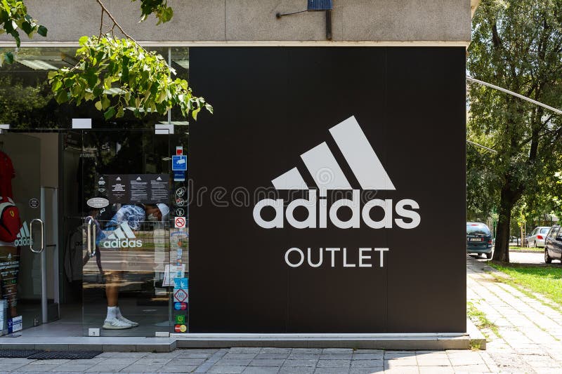 Entrada a La Tienda De Venta De Adidas Desde Una Calle De La Ciudad En Un Soleado Día De Verano. Cartel Con El Logo De Adidas Bren Imagen archivo editorial -