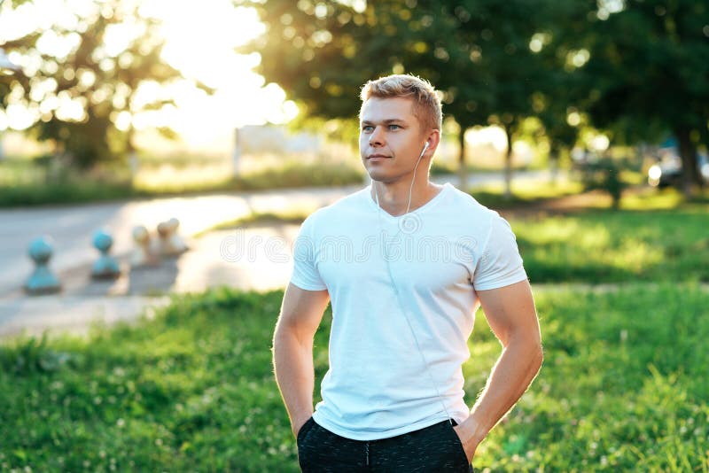 Entraîneur d'homme dans des écouteurs Dans un T-shirt blanc Sourire heureux Écoute la musique, regard sûr Mode de vie d'été photos libres de droits Entraîneur d'homme dans des écouteurs Dans un T-shirt blanc Sourire heureux Écoute la musique, regard sûr Mode de vie d'été photos libres de droits