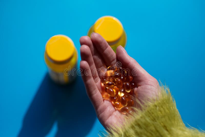 Entregando cápsulas oleosas amarelas da medicina da vitamina sobre o fundo azul foto de stock Entregando cápsulas oleosas amarelas da medicina da vitamina sobre o fundo azul foto de stock