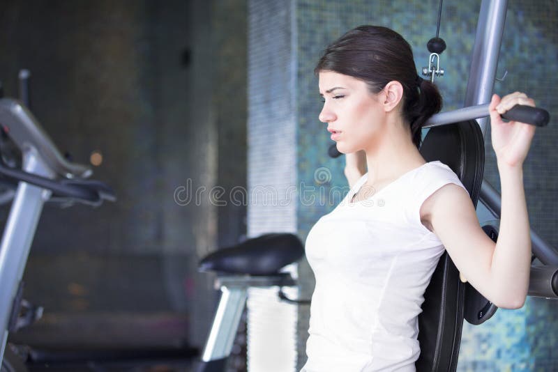 Entrenamiento del peso de la mujer en la gimnasia El ejercicio encendido tira hacia abajo la máquina del peso Mujer que hace tiró fotografía de archivo Entrenamiento del peso de la mujer en la gimnasia El ejercicio encendido tira hacia abajo la máquina del peso Mujer que hace tiró fotografía de archivo