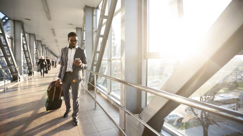 Business Travel. Entrepreneur Man Using Mobile Phone Texting Walking With Baggage In Airport Terminal. Copy Space, Panorama. Business Travel. Entrepreneur Man Using Mobile Phone Texting Walking With Baggage In Airport Terminal. Copy Space, Panorama