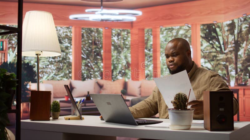 Entrepreneur taking notes and managing business analytics at his home office analyzing economic trends on a laptop freelancer imagem de stock