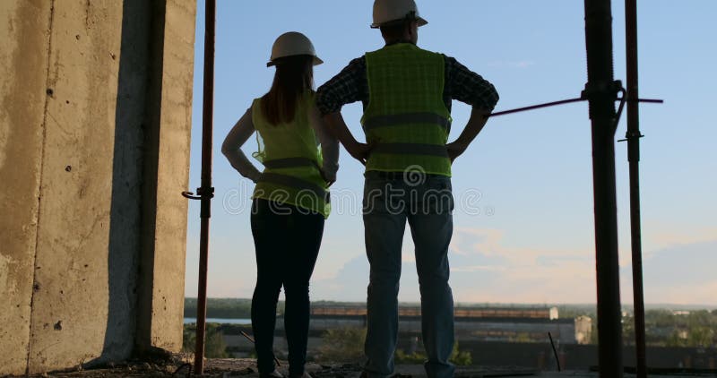 Entreprise de construction : concept de travail d'équipe : Jeune position d'ingénieur derrière regarder un chantier, portant une