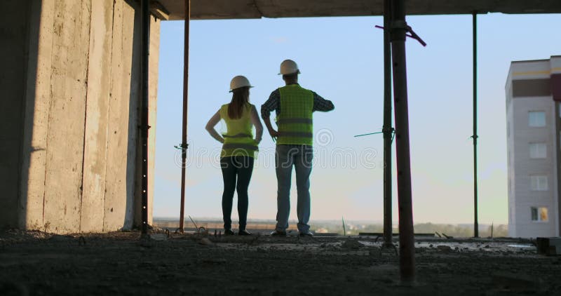 Entreprise de construction : concept de travail d'équipe : Jeune position d'ingénieur derrière regarder un chantier, portant une