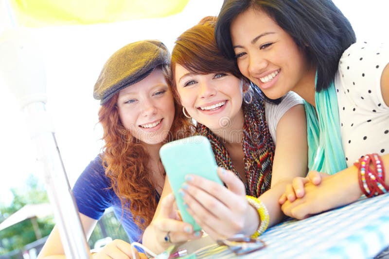 Smartphone entertainment. A group of adolescent girls laughing as they look at something on a smartphone screen. Smartphone entertainment. A group of adolescent girls laughing as they look at something on a smartphone screen