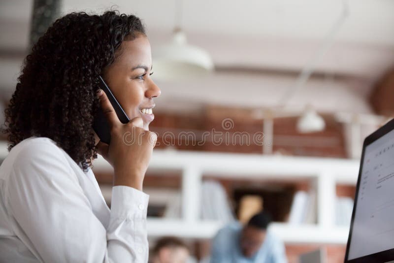 Entretien femelle noir de sourire des employés au téléphone fonctionnant à l'ordinateur photographie stock Entretien femelle noir de sourire des employés au téléphone fonctionnant à l'ordinateur photographie stock