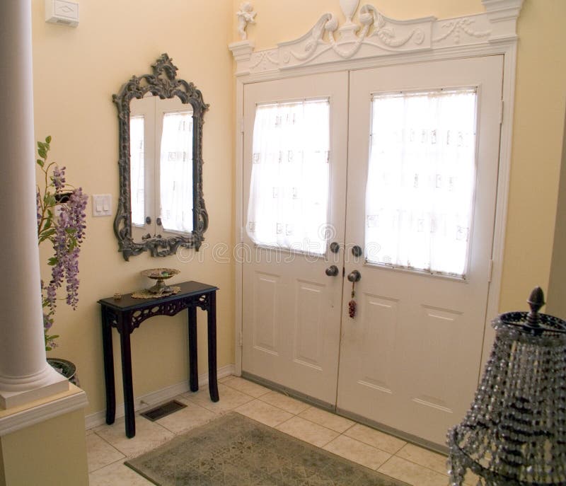 Entry Hall 09. Ornate Entry Hall of a house with white windowed doors, columns, wall mirror and key table with a tile floor and rug Entry Hall 09. Ornate Entry Hall of a house with white windowed doors, columns, wall mirror and key table with a tile floor and rug