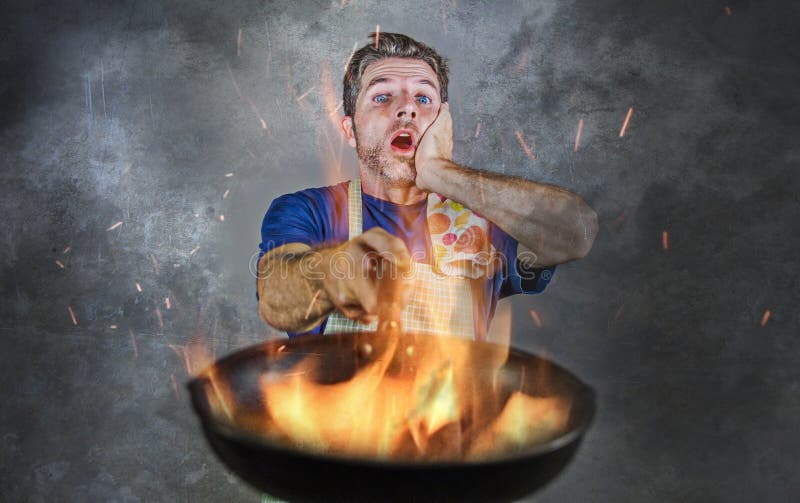 Entsetzter unordentlicher Mann mit dem Schutzblech, das Wanne im Feuer brennt das Lebensmittel im Küchenunfall und in unerfahrene stockbild Entsetzter unordentlicher Mann mit dem Schutzblech, das Wanne im Feuer brennt das Lebensmittel im Küchenunfall und in unerfahrene stockbild