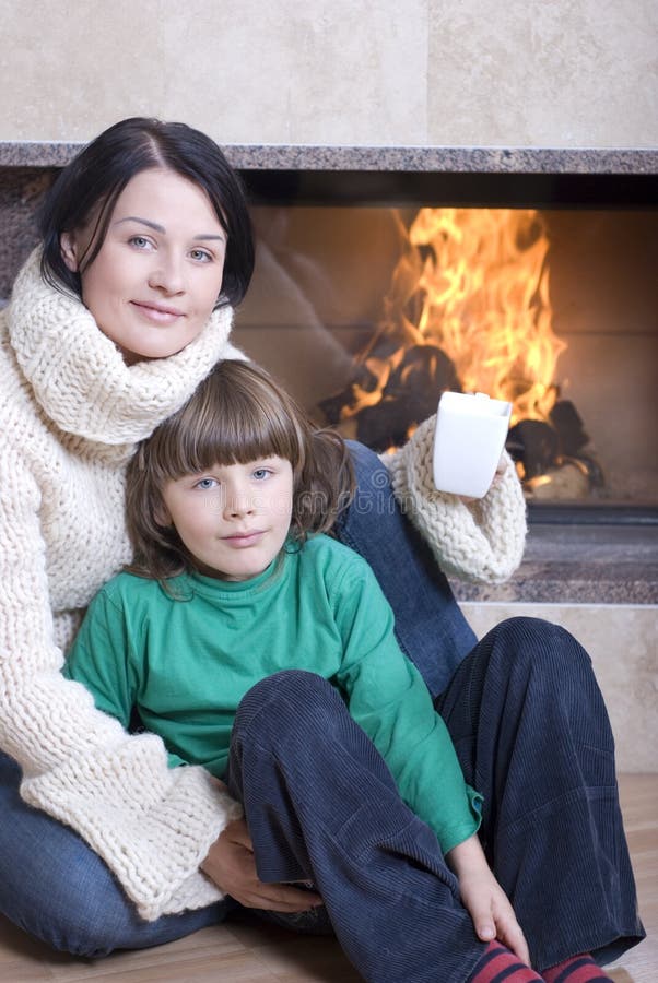 Attractive mother drinking a cup of hot coffee sitting in front of a fireplace. Attractive mother drinking a cup of hot coffee sitting in front of a fireplace