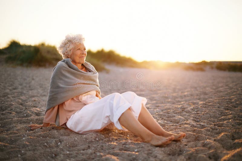 Entspannte ältere Frau, die auf dem Strand sitzt stockbild