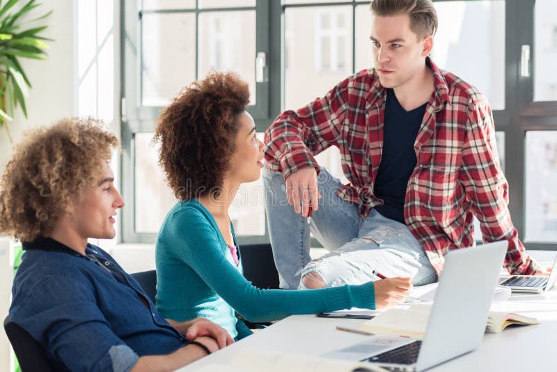 Entspannter junger Student, der mit seinen Mitschülern während des Bruches spricht stockfotografie Entspannter junger Student, der mit seinen Mitschülern während des Bruches spricht stockfotografie