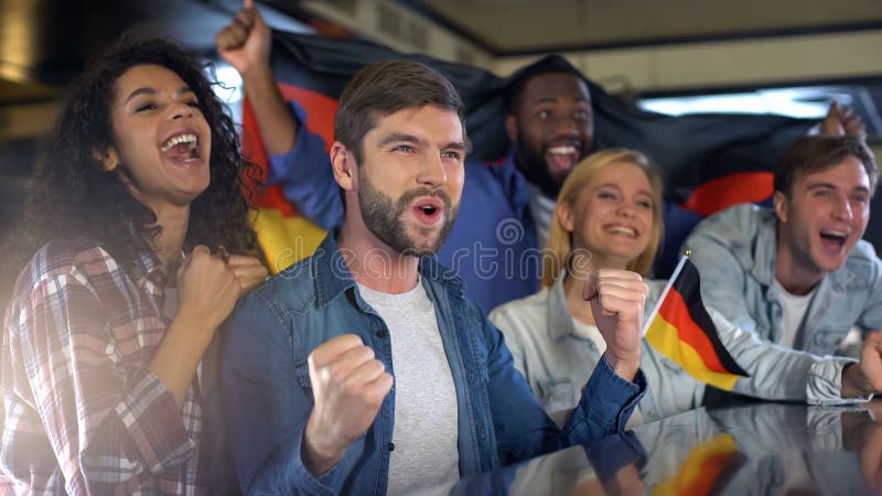 Entusiastisk tysk flagga för innehav för sportfans som är lycklig om landslagseger royaltyfria foton Entusiastisk tysk flagga för innehav för sportfans som är lycklig om landslagseger royaltyfria foton