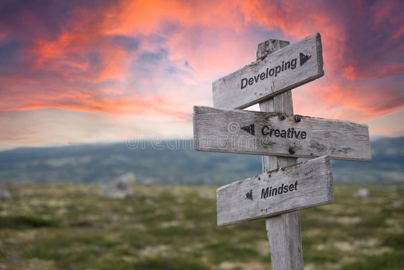 Developing creative mindset text engraved in wooden signpost outdoors in nature during sunset and pink skies. Developing creative mindset text engraved in wooden signpost outdoors in nature during sunset and pink skies