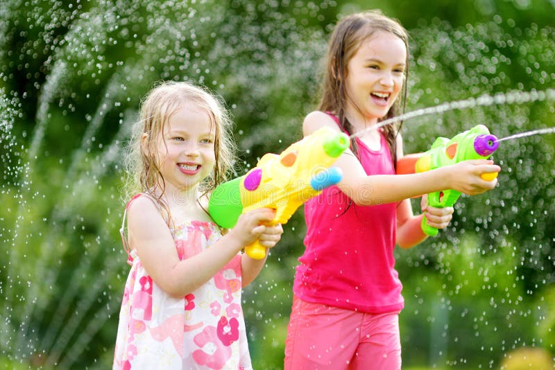 Entzückende kleine Mädchen, die mit Wasserwerfern am heißen Sommertag spielen Nette Kinder, die Spaß mit Wasser draußen haben