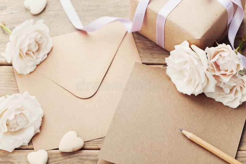 Envelope or letter, gift, paper card and vintage rose flowers on rustic wooden table for greeting on Mother or Woman Day.